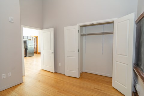 A room with white walls and wooden floors, with a doorway leading to another room.
