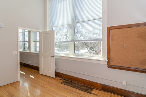 A room with a white door, a window with blinds, and a corkboard on the wall.