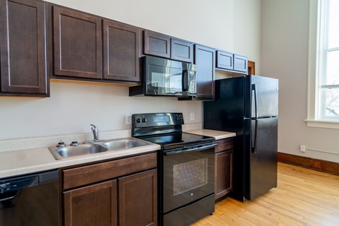 A black refrigerator is in a kitchen with wooden cabinets.