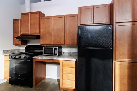 A black refrigerator sits in a kitchen with wooden cabinets.