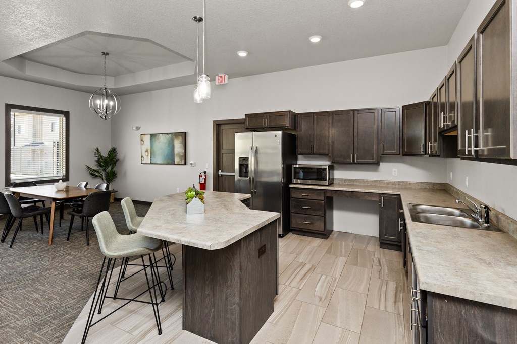A kitchen with a table and chairs in the foreground and a refrigerator, microwave, and oven in the background.