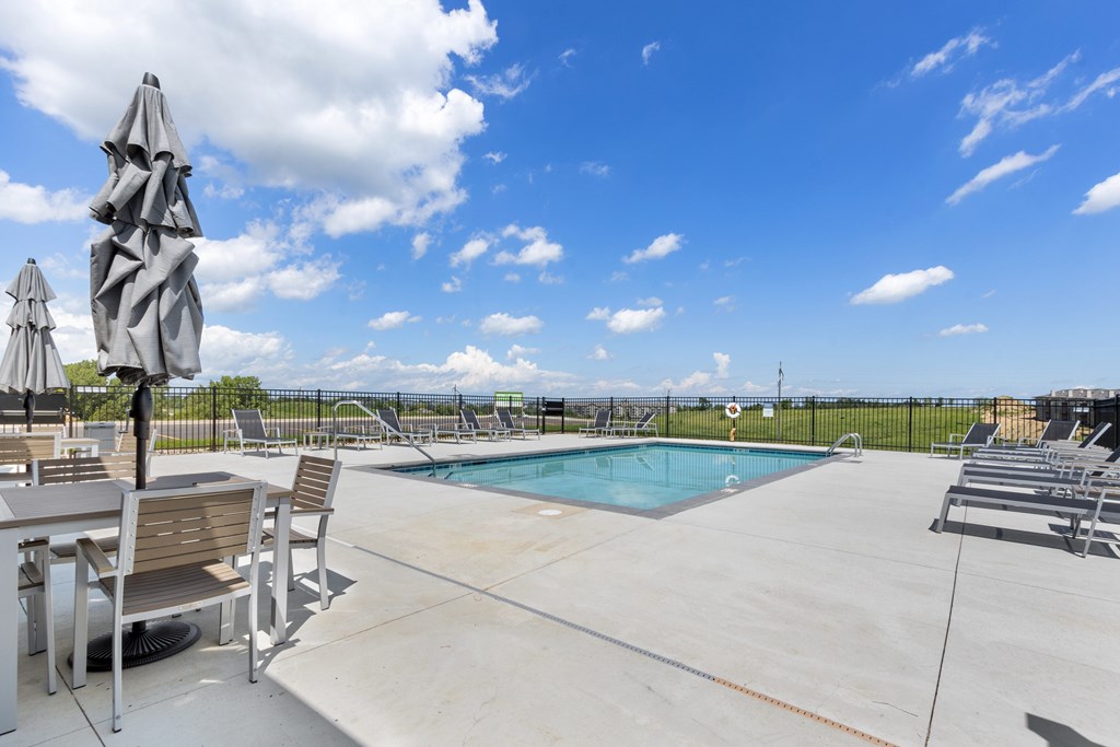 A pool area with a table and chairs and a blue pool.
