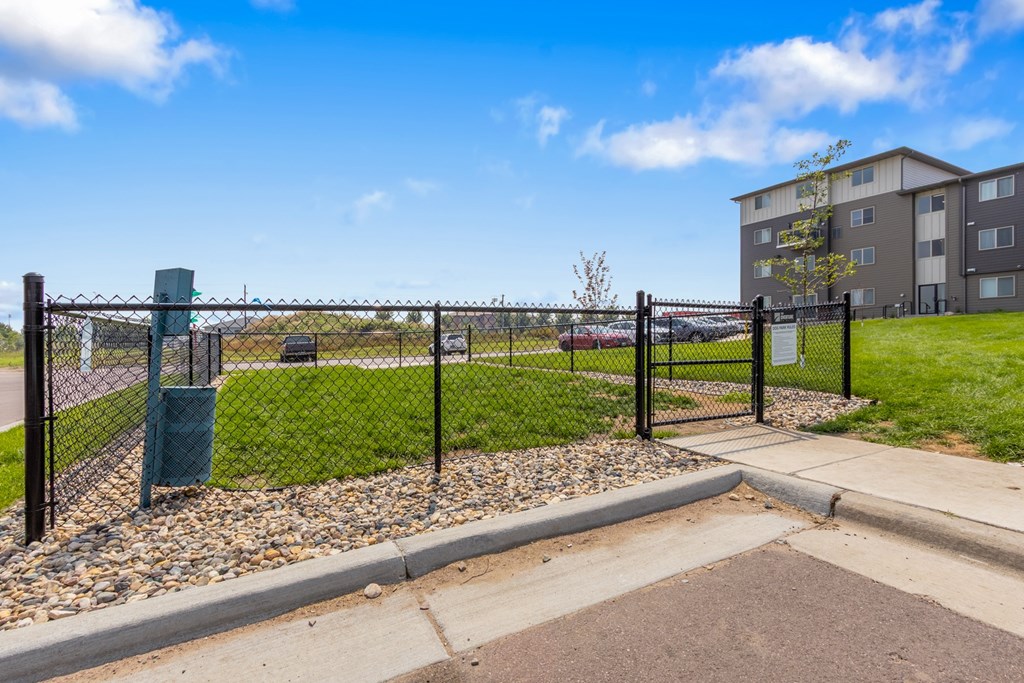 A black fence surrounds a green trash can next to a sidewalk.