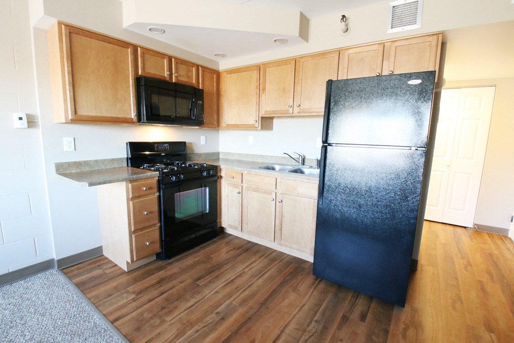 an empty kitchen with wood flooring and a black refrigerator