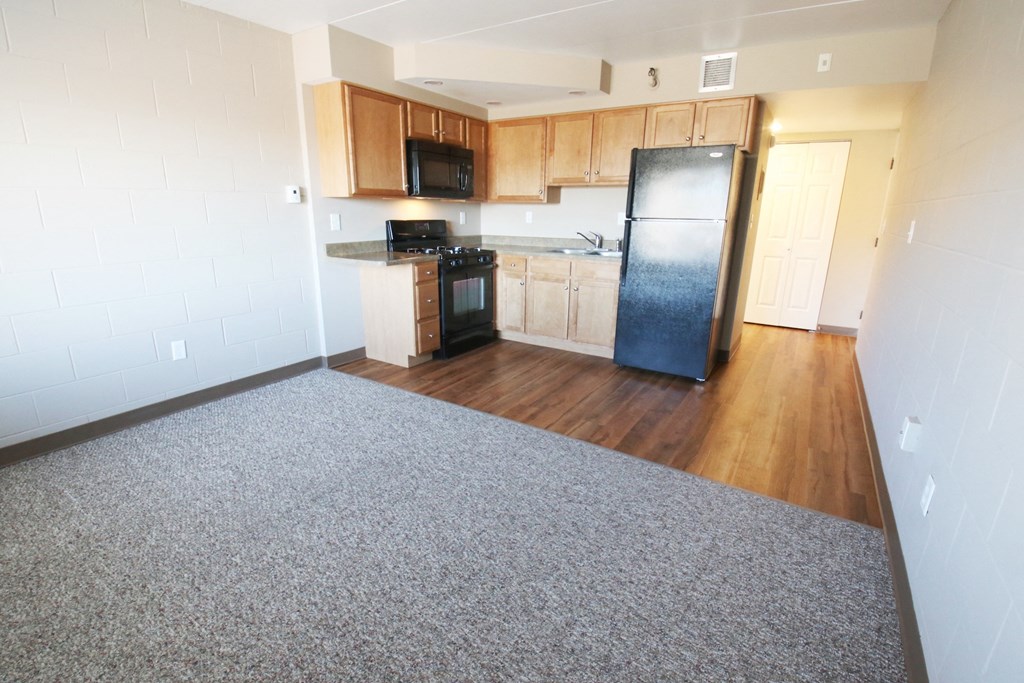 an empty kitchen with wood floors and a black refrigerator