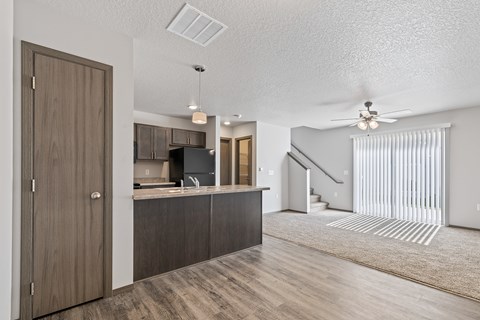 A modern kitchen with wooden cabinets and a staircase in the background.
