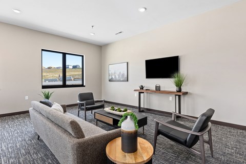 A living room with a grey couch, a black chair, a wooden coffee table, and a flat screen TV mounted on the wall.