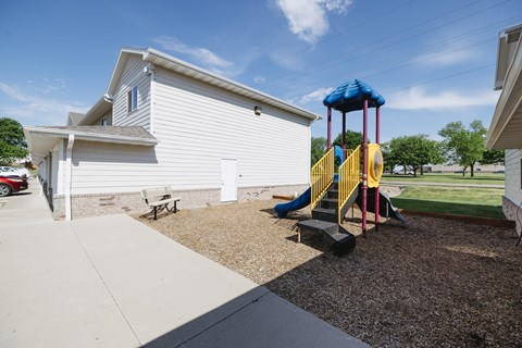 A playground with a slide and a white house in the background.