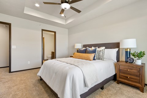 A bedroom with a large bed, a ceiling fan, and a nightstand with a plant on it.