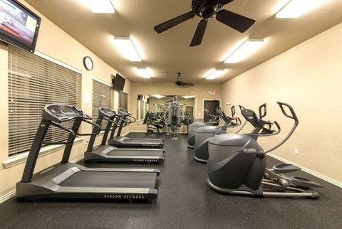 a gym with cardio machines and a ceiling fan