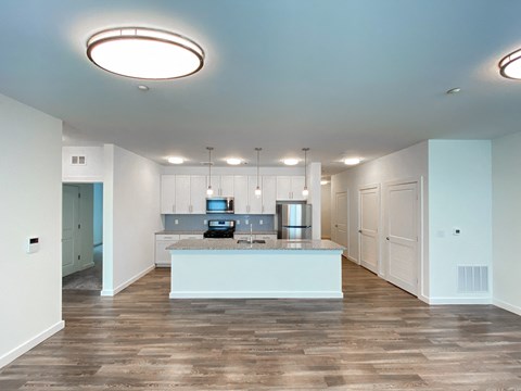 an empty living room with a kitchen with white cabinets and a counter top
