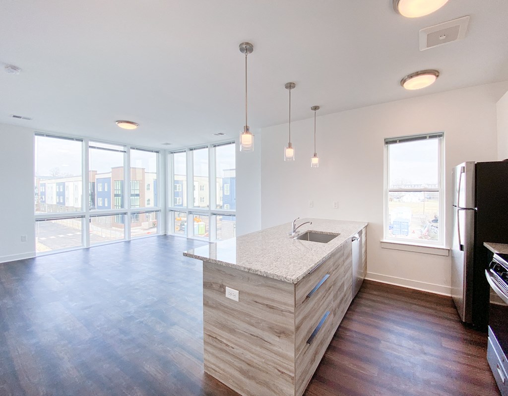 an empty living room with a kitchen and a large window