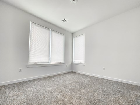 an empty bedroom with two windows and a carpeted floor