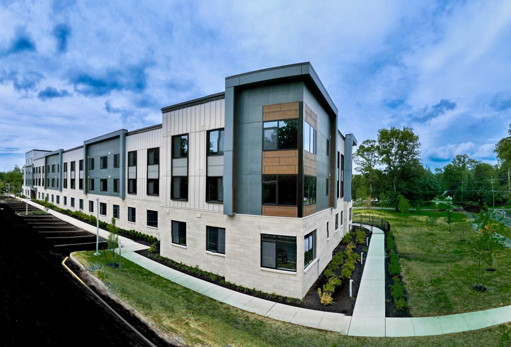 A modern building with a curved design and large windows is surrounded by a well-maintained lawn and a paved walkway.