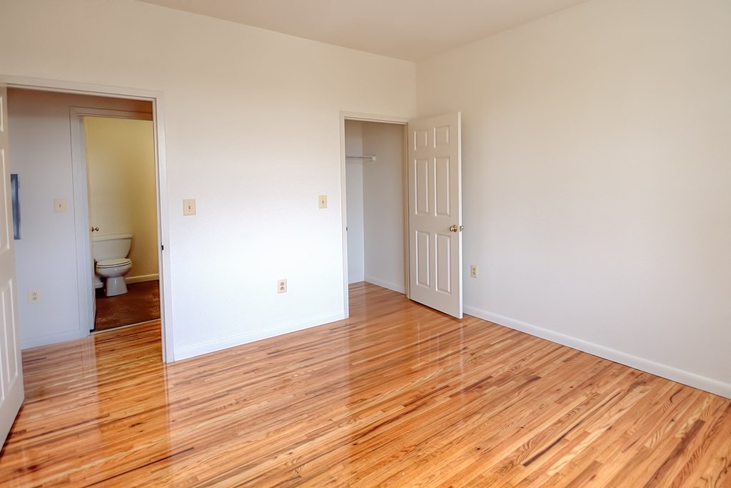 an empty living room with wood flooring and a door to a bathroom