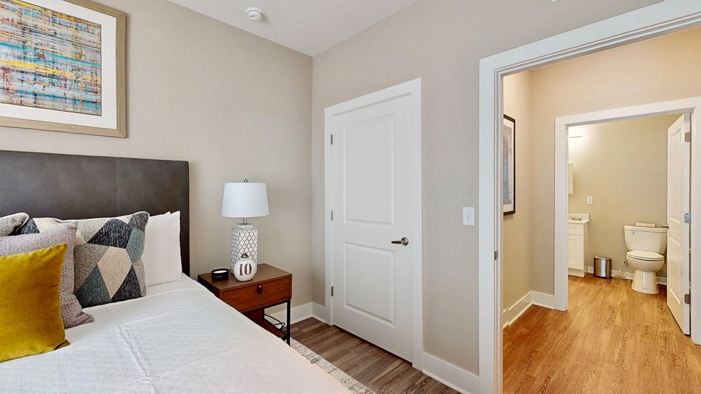 A bedroom with a bed, nightstand, and a bathroom in the background.