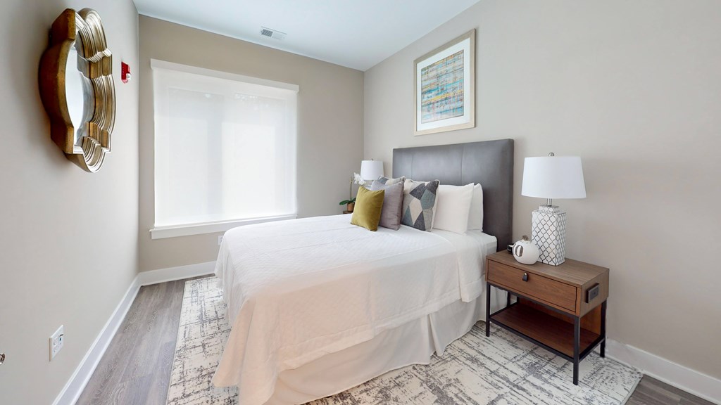 A bedroom with a large bed, a nightstand, and a mirror on the wall.