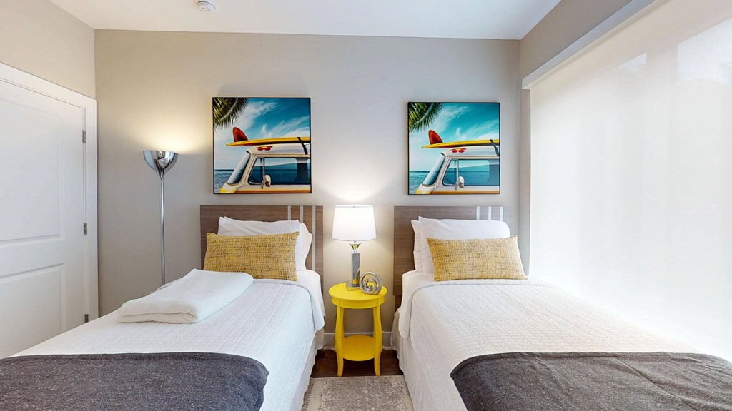 Two twin beds in a room with yellow side tables and beach-themed pictures on the wall.