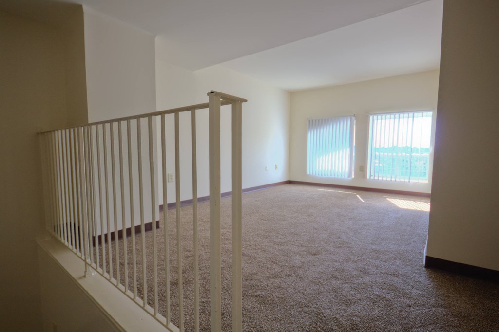 an empty living room with white carpet and a staircase