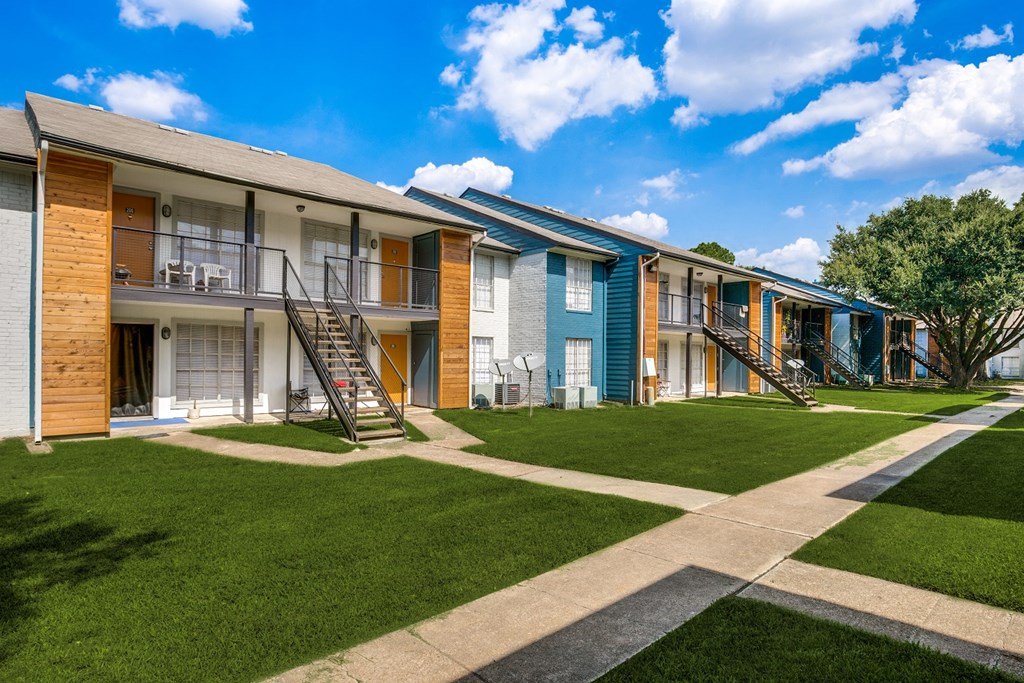an exterior view of a row of apartments with grass and a sidewalk