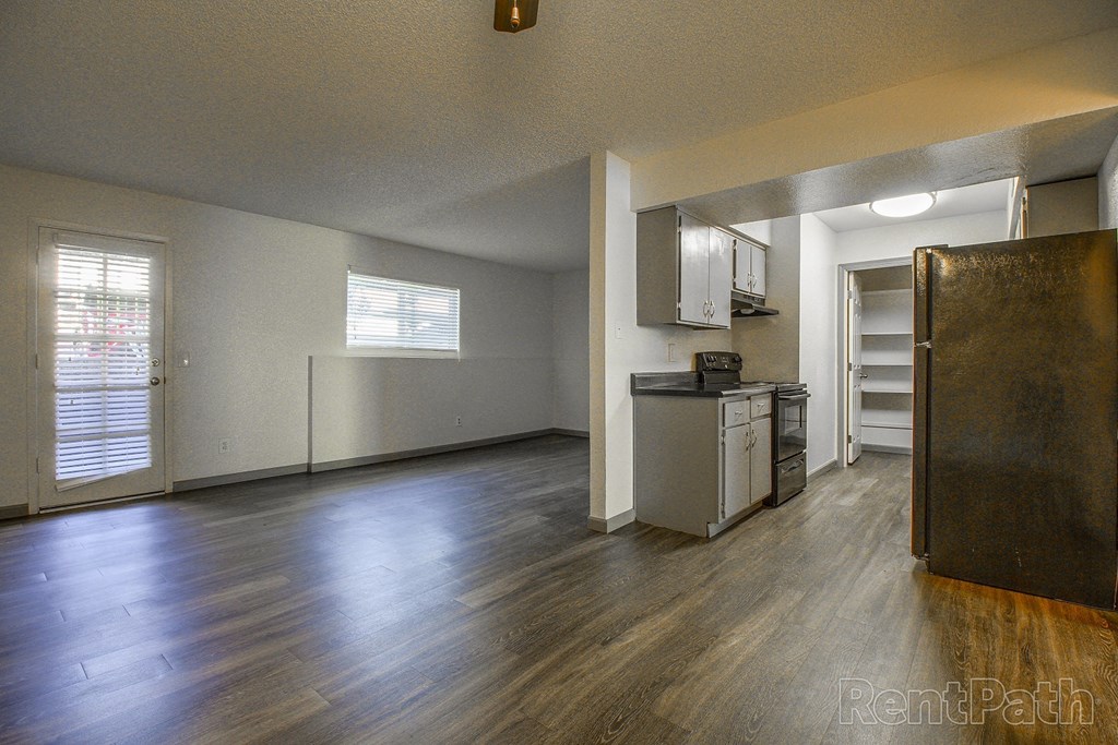 an empty living room with wood floors and a kitchen