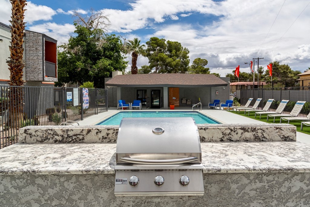 a grill in front of a pool with chairs and a house