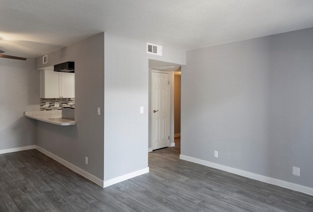 the living room and kitchen of an apartment with gray walls and wood flooring