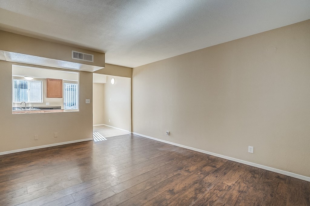 an empty living room with wood floors and a kitchen