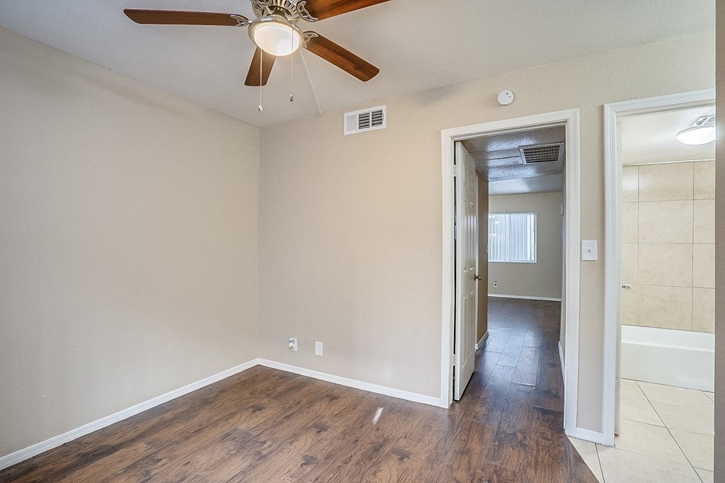 an empty living room with a ceiling fan and a hallway
