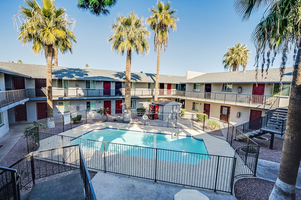 a swimming pool is surrounded by palm trees in front of an apartment building