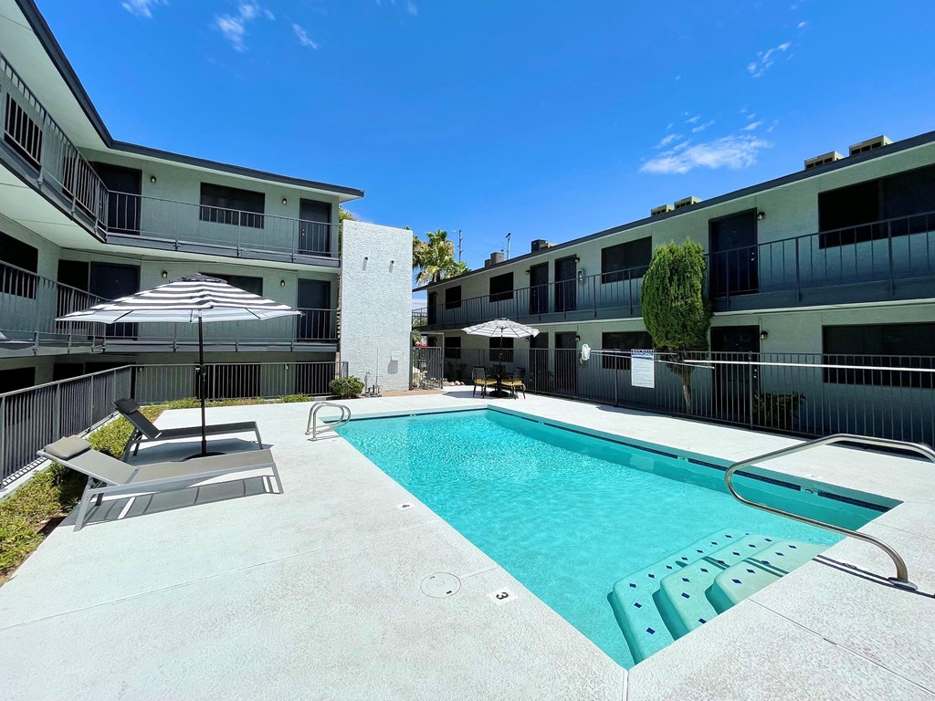 a swimming pool with lounge chairs and umbrellas in front of a building