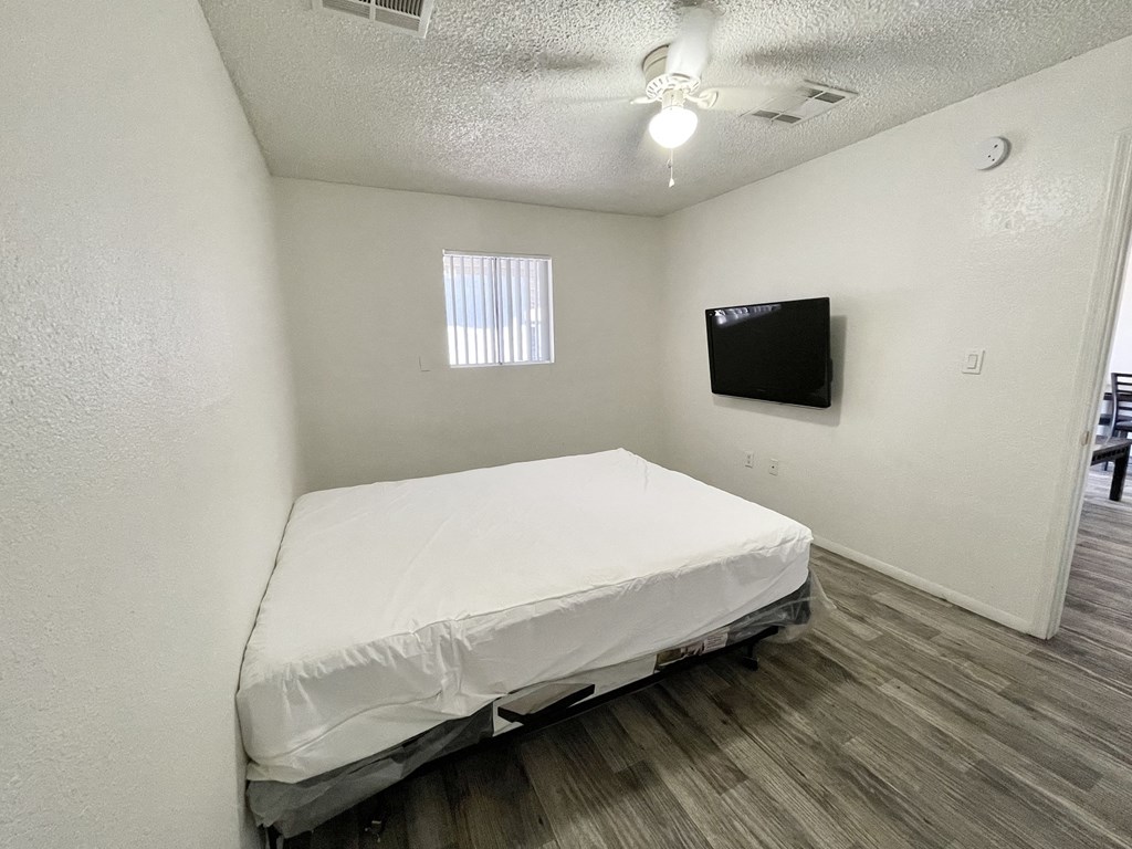an empty bedroom with a bed and a tv on the wall