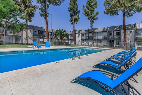 a swimming pool at an apartment building with blue lounge chairs