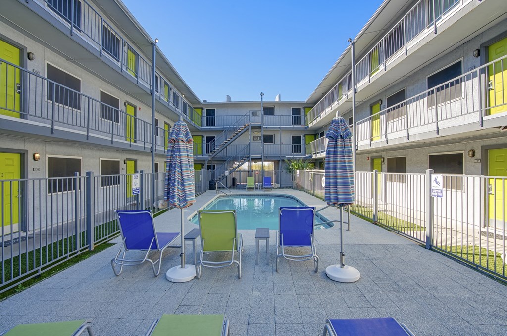 a swimming pool with chairs and umbrellas in front of an apartment building