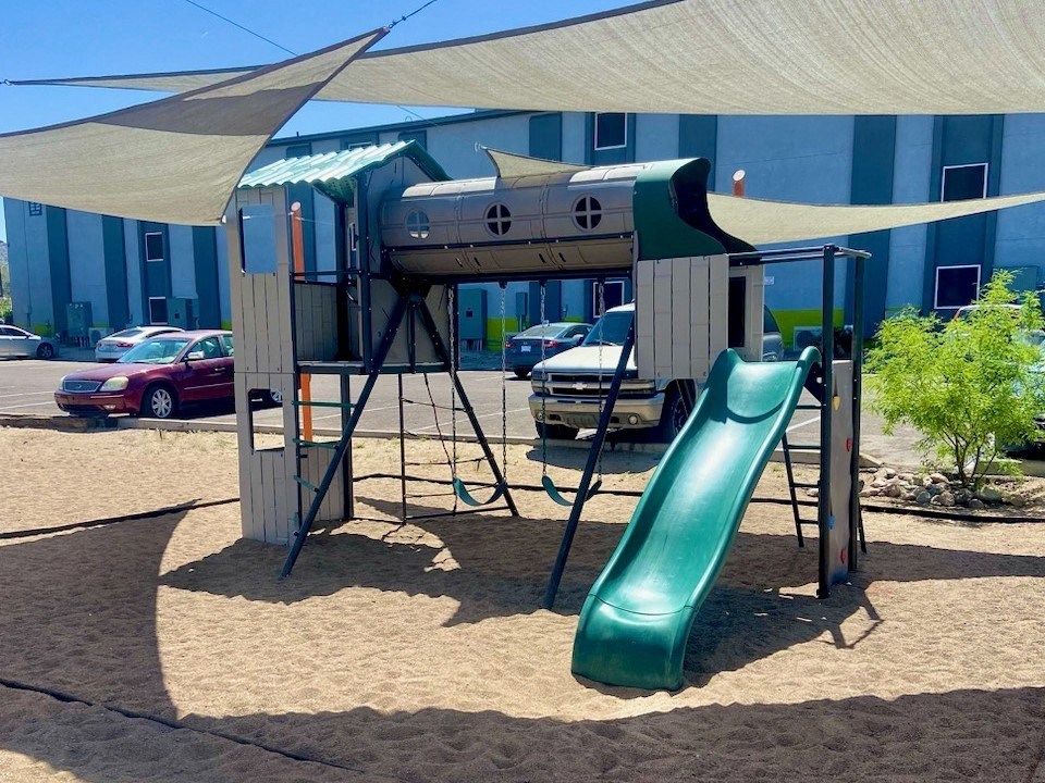 a swing set with a slide in a parking lot with a building in the background