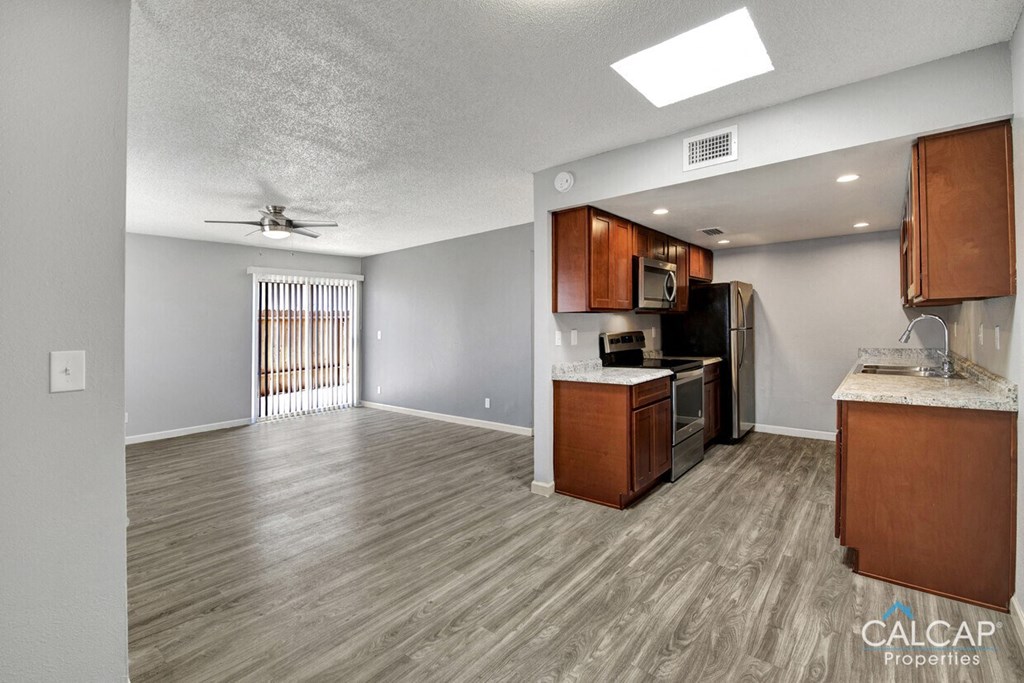 an empty living room with a kitchen and a ceiling fan