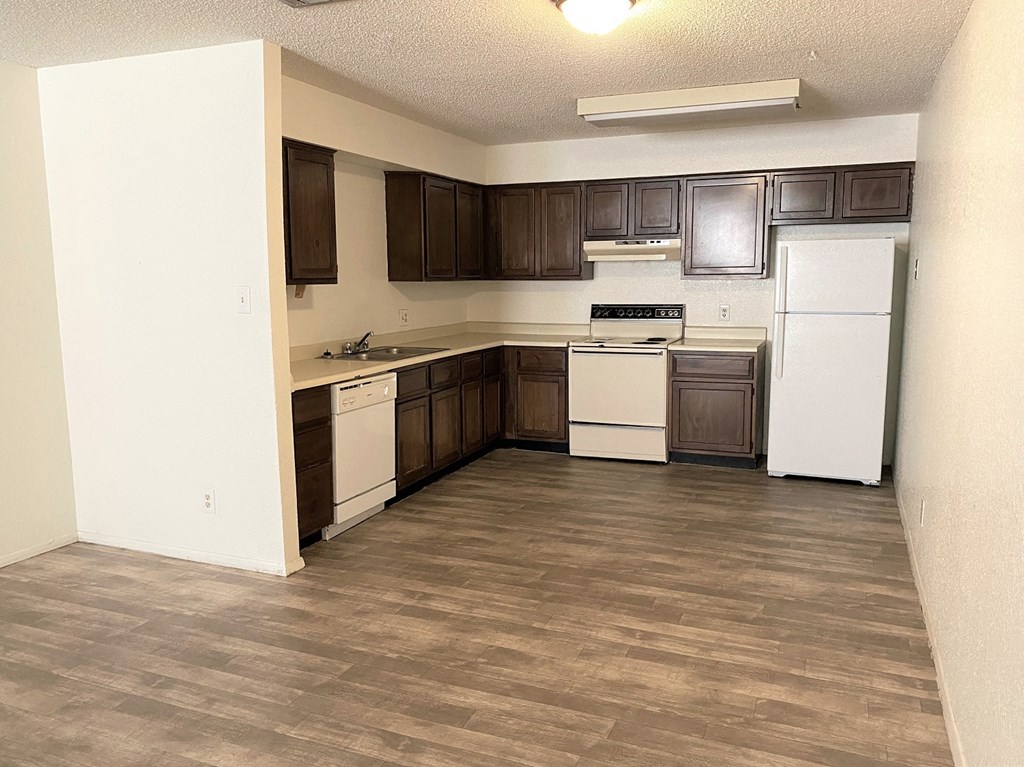 an empty kitchen with white appliances and dark wood cabinets
