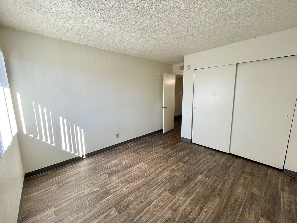 a bedroom with white walls and wood flooring and a closet