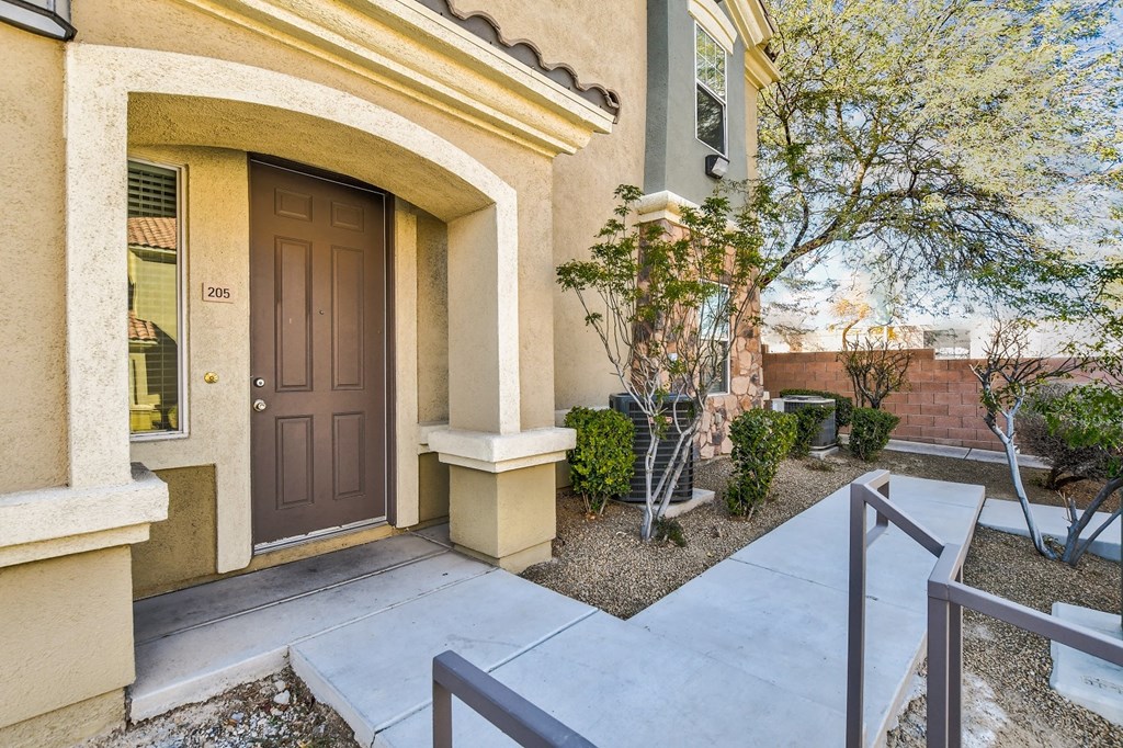 the front door of a beige home with a brown door and a porch