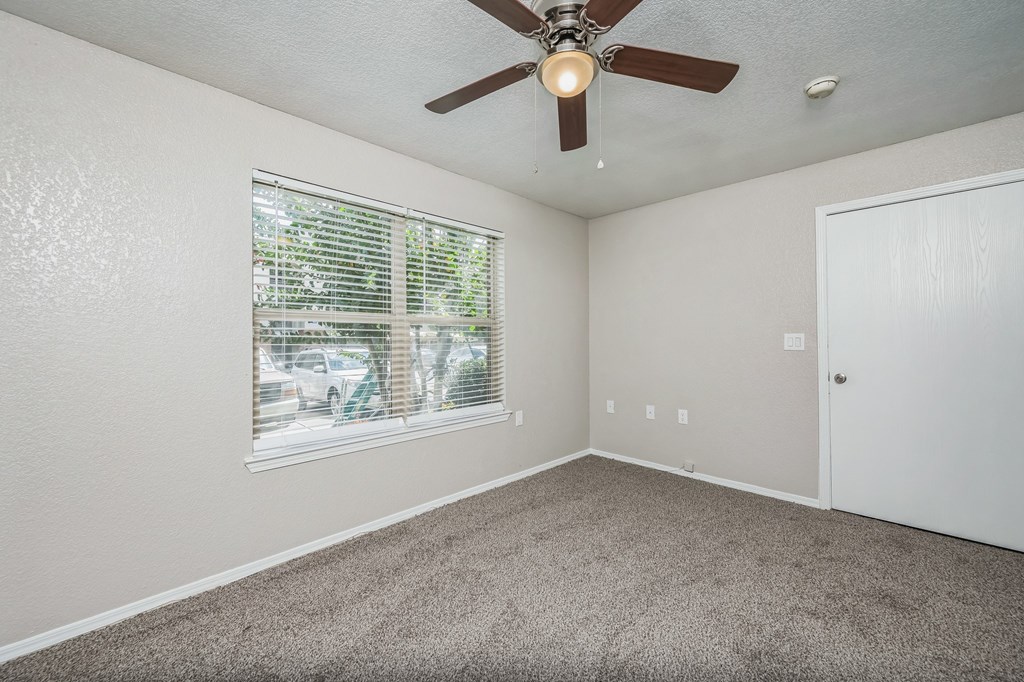 an empty living room with a ceiling fan and windows