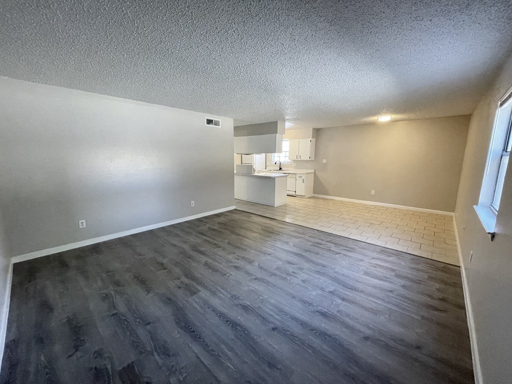 an empty living room with wood flooring and a kitchen