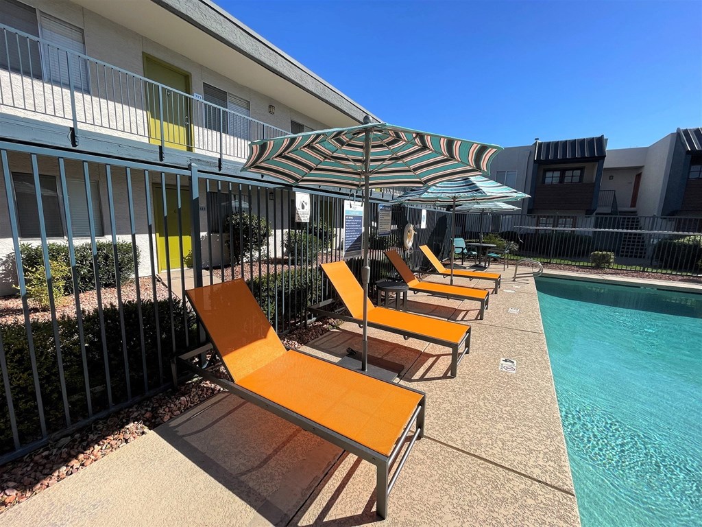 a row of orange lounge chairs and an umbrella next to a pool