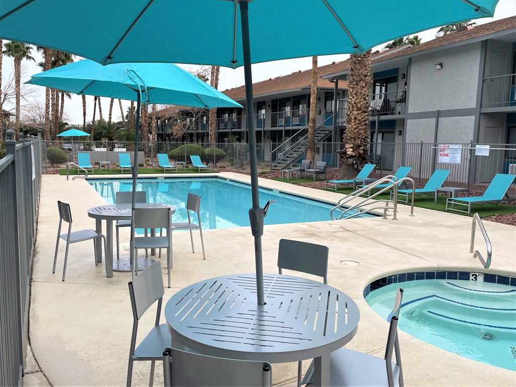 a swimming pool with tables and umbrellas in front of a hotel
