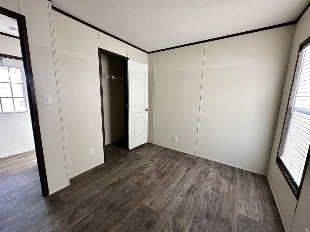 a bedroom with white walls and wood flooring and a closet