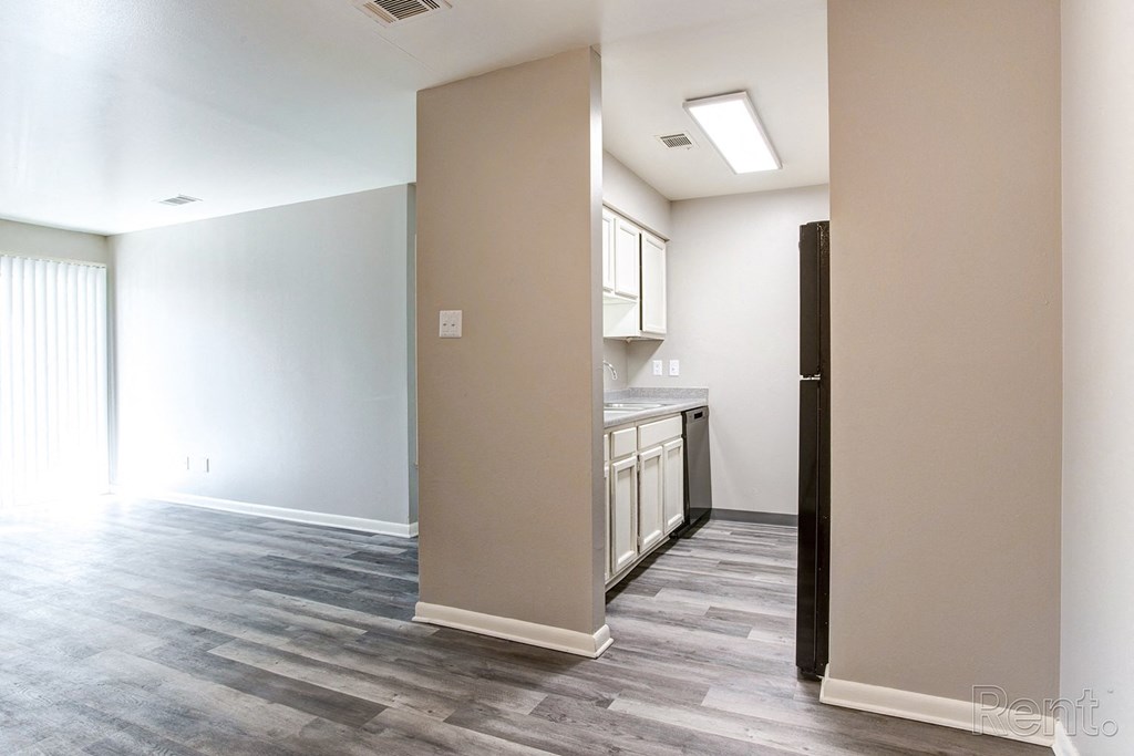 an empty living room and kitchen with wood flooring and white walls