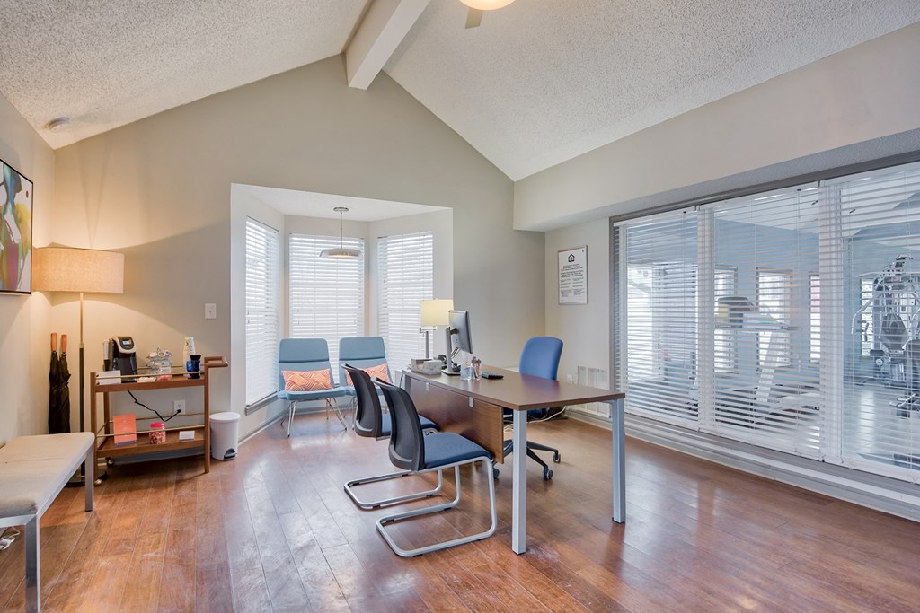a room with a desk and chairs and a large window with blinds