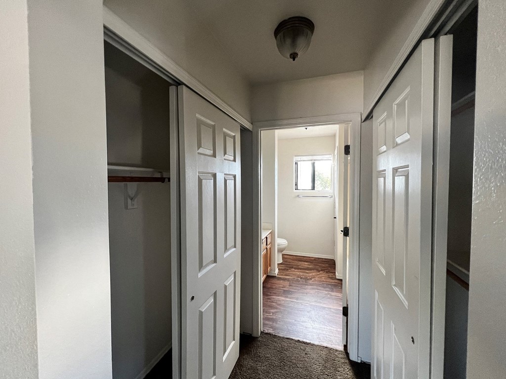 a hallway with two closets and a door open to a bedroom and a bathroom
