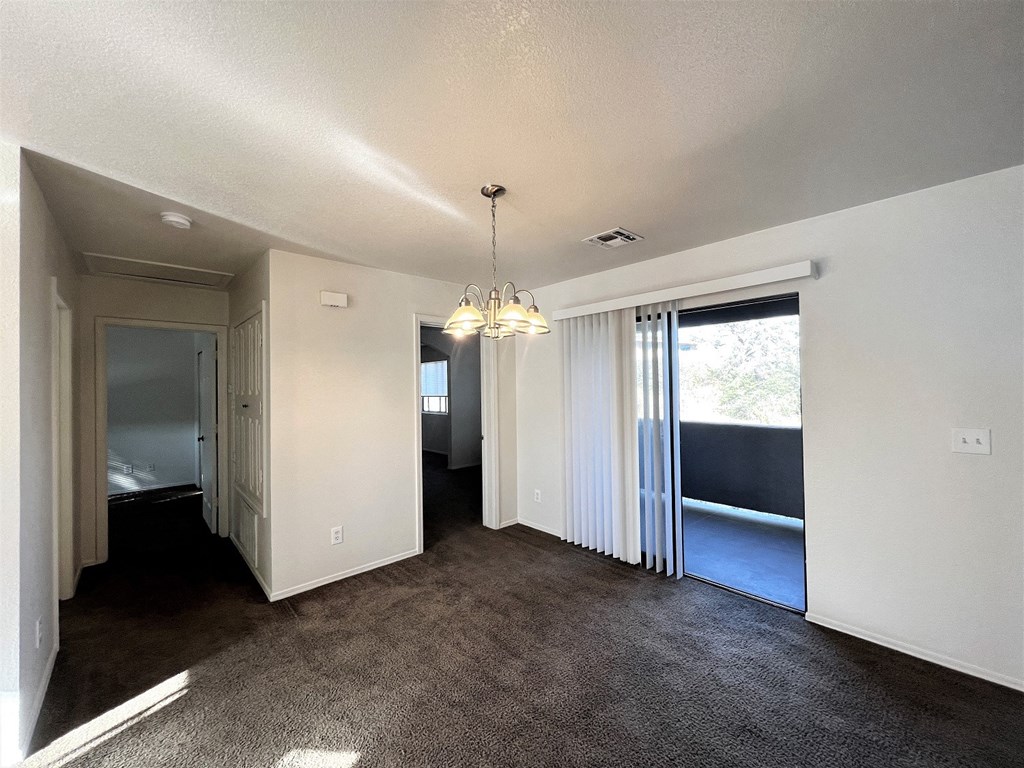 an empty living room with a chandelier and a door to a bedroom