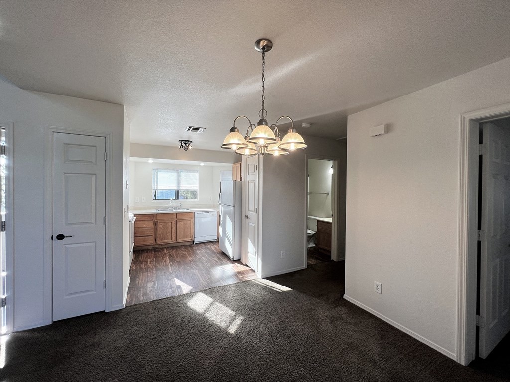 an empty living room with a kitchen in the background
