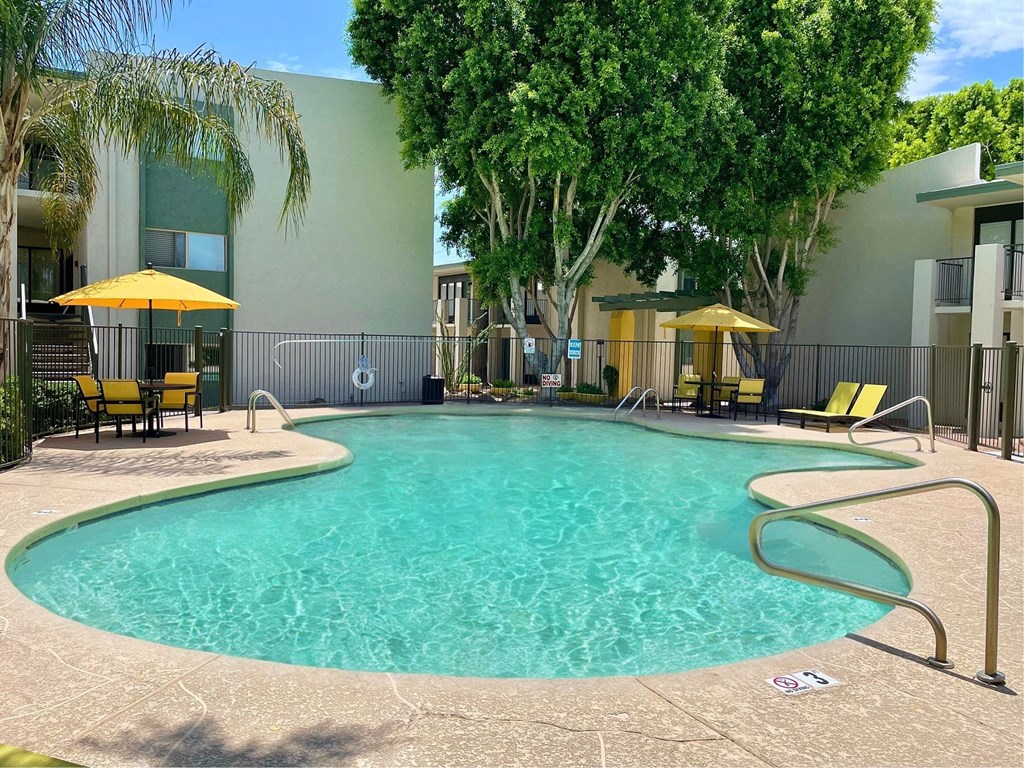 a resort style swimming pool with yellow chaise lounges and umbrellas